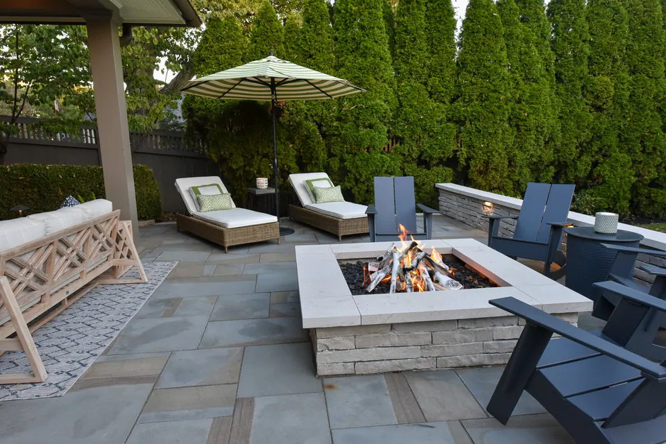 Square firepit with chairs, covered patio, paver terrace, umbrella, and privacy planting